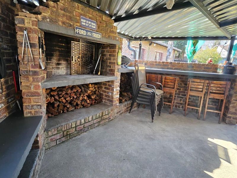Covered outdoor patio area featuring a substantial built-in brick braai, concrete prep surfaces, and a durable corrugated metal roof structure.