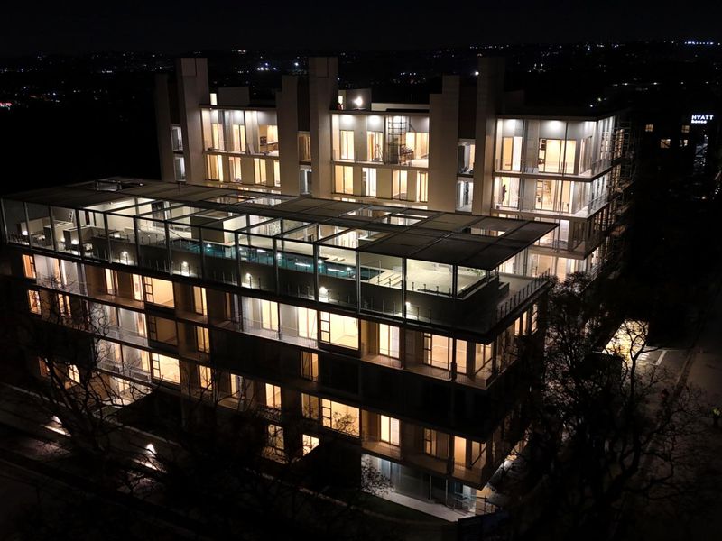 Nighttime aerial view of a modern multi-story apartment building featuring a rooftop swimming pool and illuminated balconies.