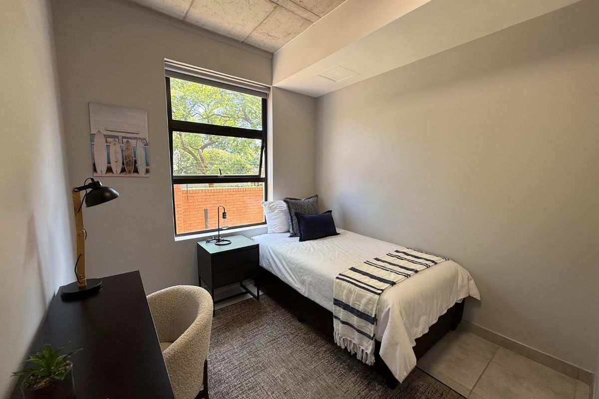 A modern bedroom featuring an exposed concrete ceiling, tiled flooring, and a large window providing natural light.