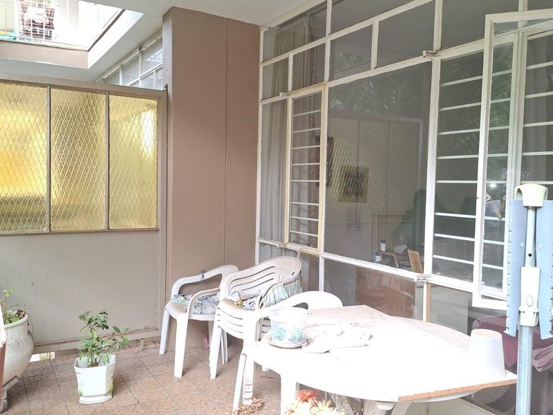 A covered balcony area featuring tiled flooring, large glass windows, and a metal security screen, providing a functional outdoor space for the apartment.