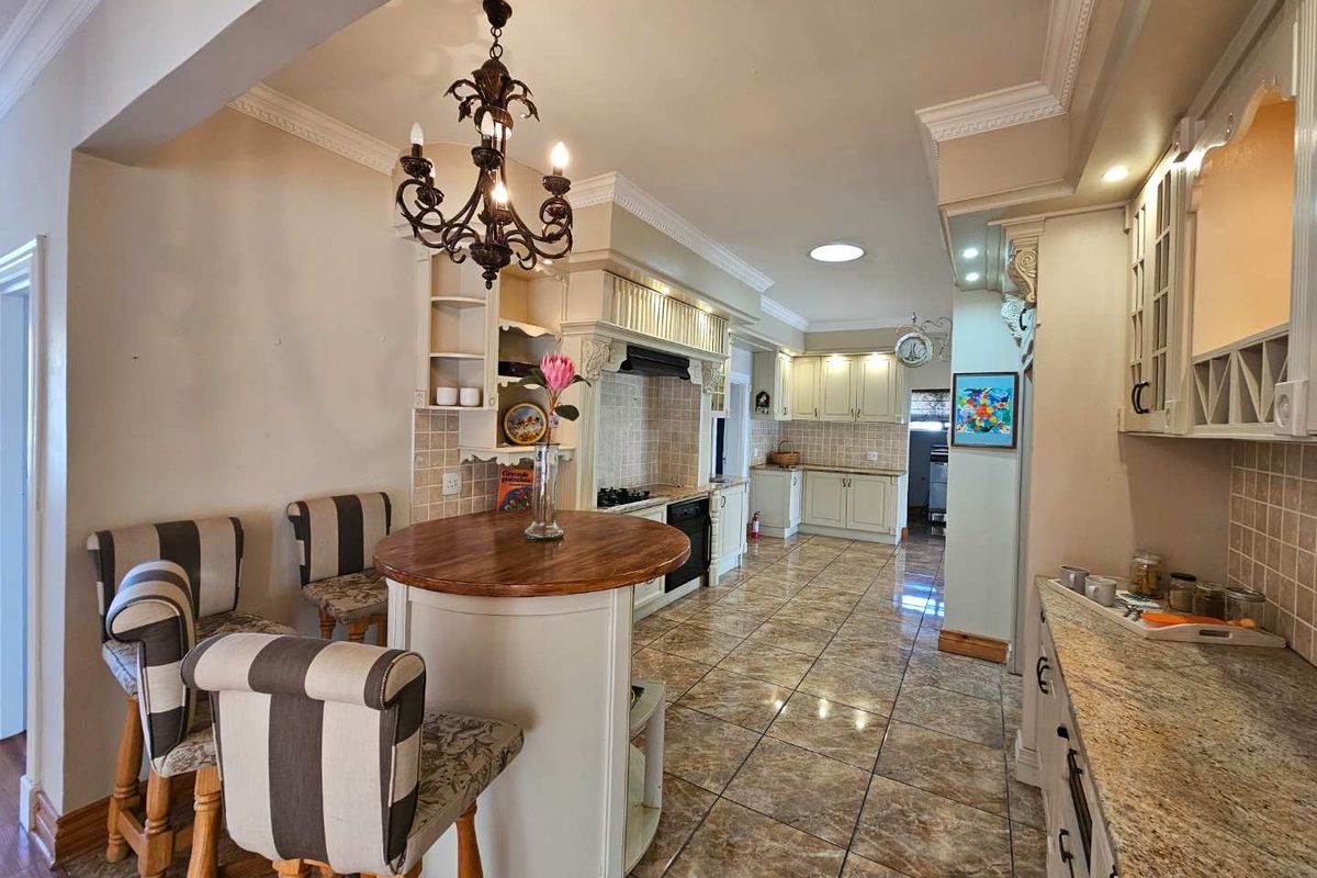 Spacious kitchen featuring granite countertops, extensive built-in cabinetry, tiled flooring, and a central breakfast nook with a decorative chandelier.