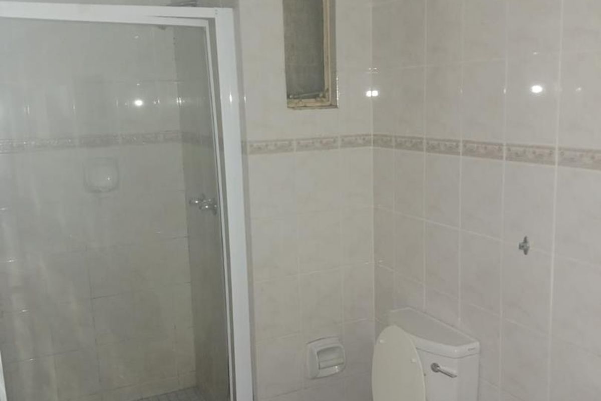 A functional bathroom featuring a glass-enclosed shower, a standard toilet, and a vanity basin with tiled walls and flooring.
