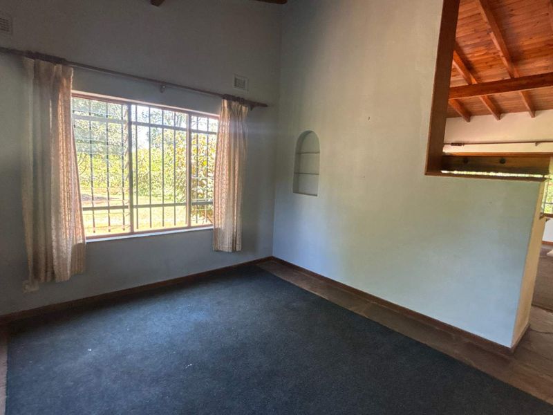 Spacious living area featuring exposed timber ceiling beams, an arched wall niche, and a combination of carpet and stone tile flooring.