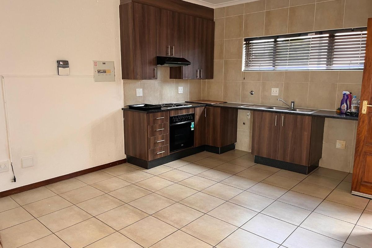 Functional kitchen featuring dark wood cabinetry, tiled splashbacks, built-in oven and hob, and a double sink with tiled flooring throughout.