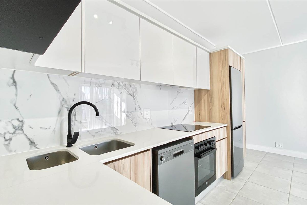 Modern kitchen featuring sleek white cabinetry, wood-grain accents, marble-look splashback, integrated sink, and built-in oven with hob.