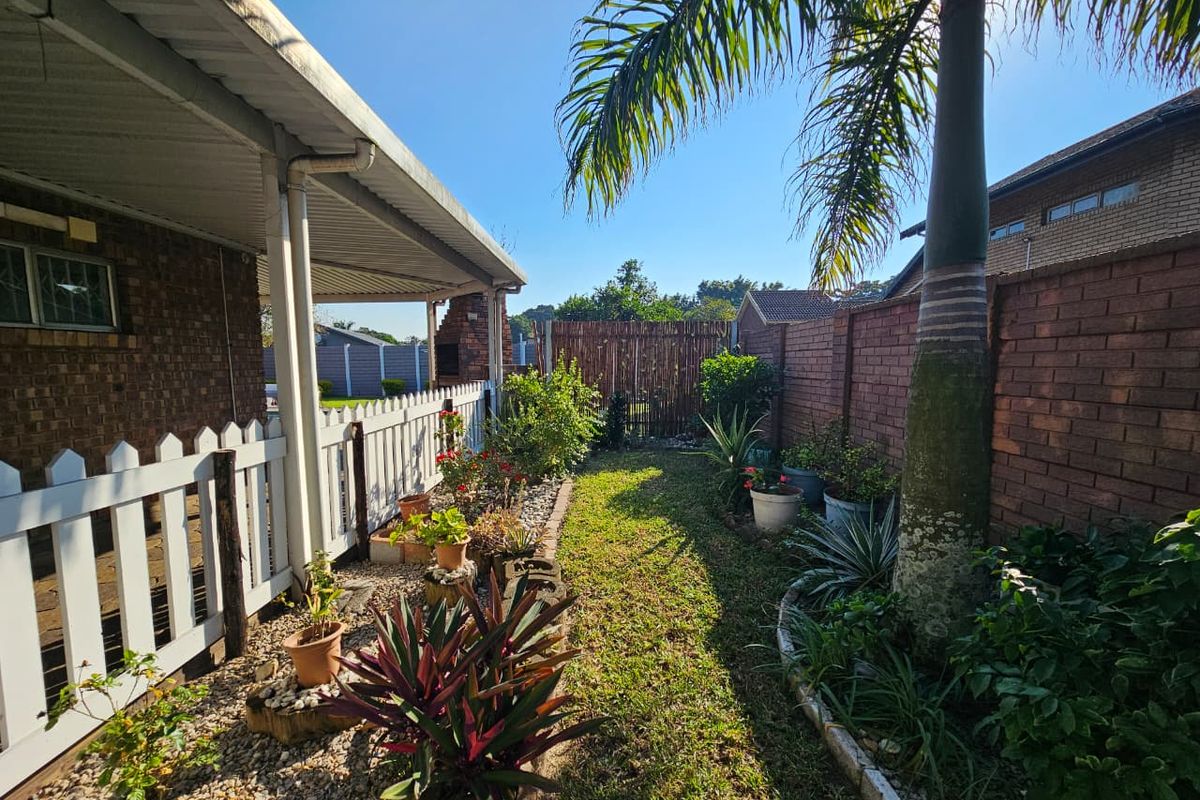 A well-maintained rear garden featuring a covered patio area, brick boundary walls, established landscaping, and a mature palm tree.