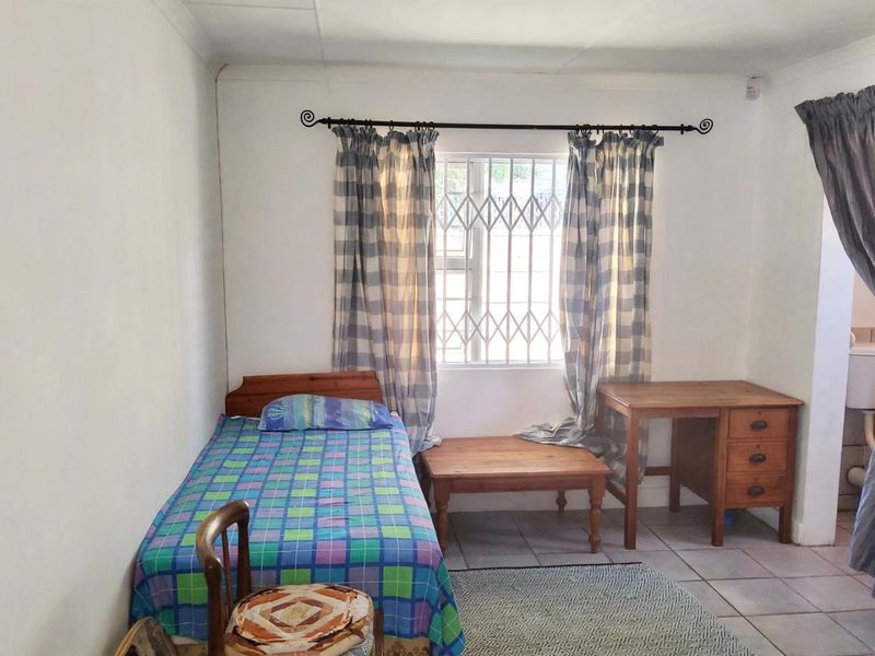 A functional bedroom featuring tiled flooring, a window with a security gate, and coving detail.