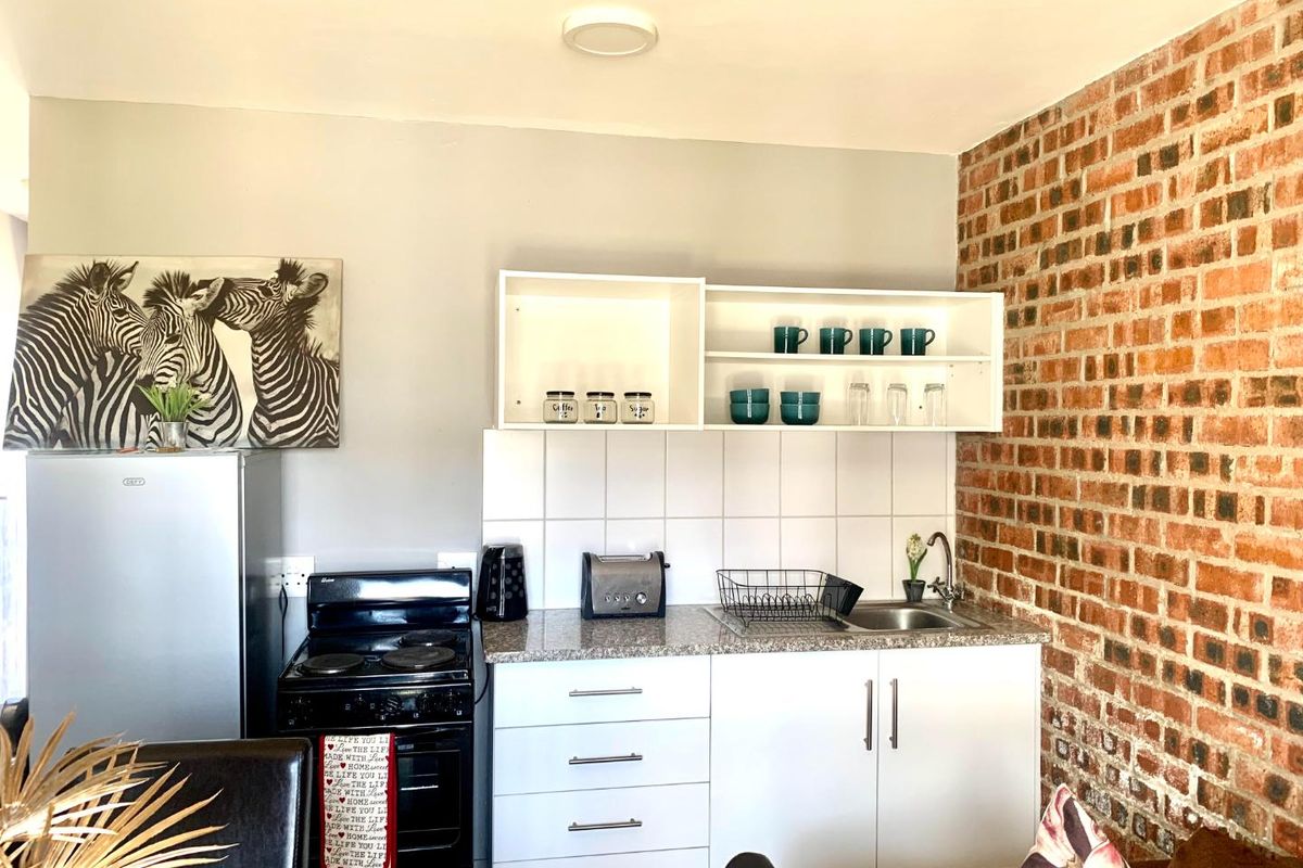Compact kitchen featuring white cabinetry, granite-look countertops, tiled backsplash, and an exposed brick feature wall.
