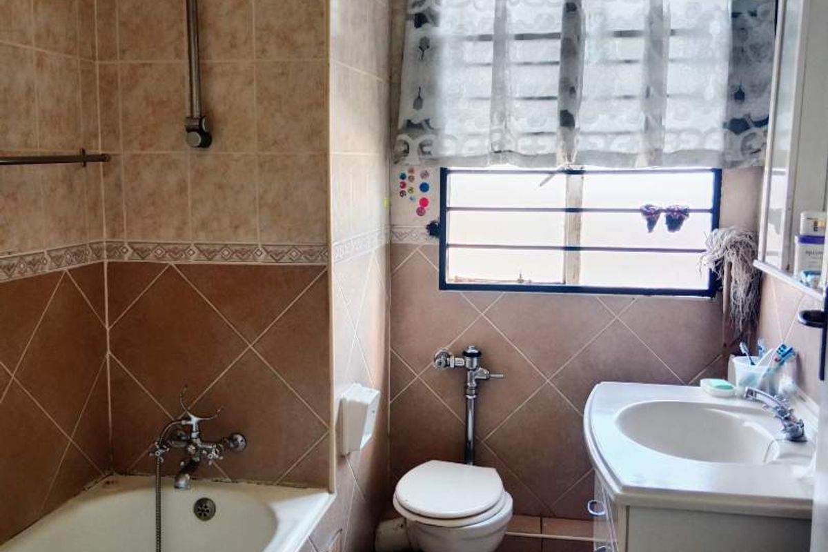 A compact bathroom featuring a bathtub with shower mixer, vanity basin, and toilet, finished with dated wall and floor tiling.