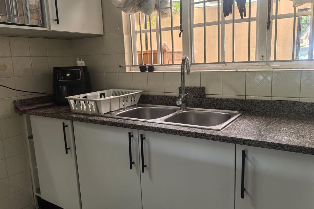 A functional kitchen area featuring a double bowl stainless steel sink, granite countertops, tiled backsplash, and white cabinetry with modern hardware.