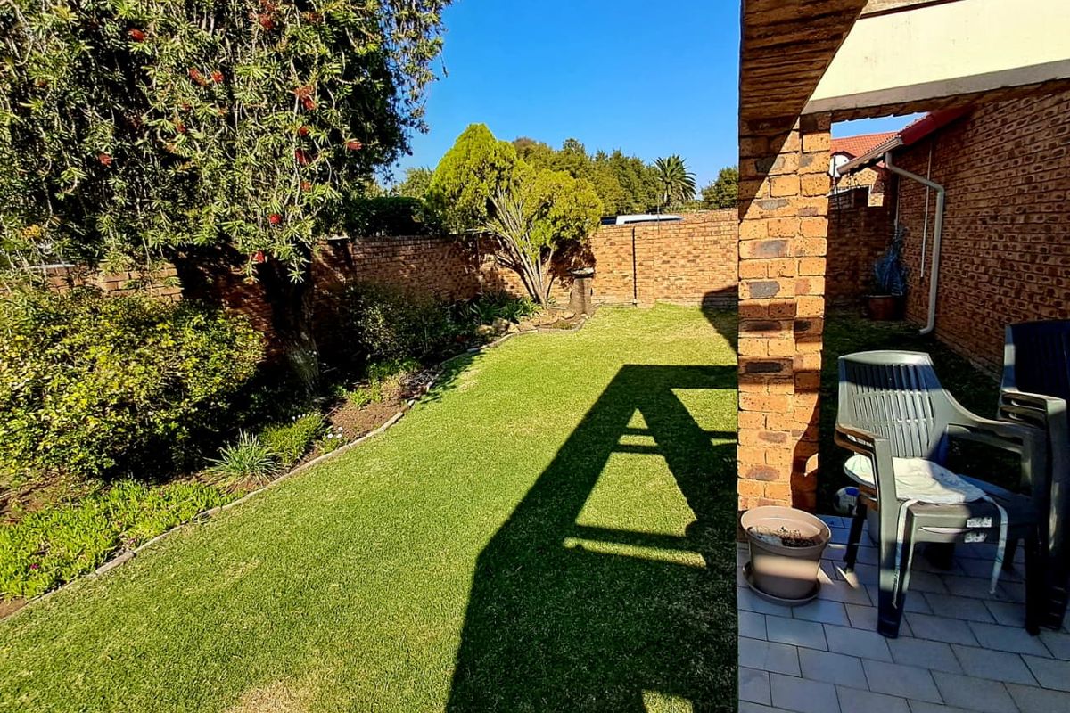 A private rear garden featuring a paved patio area, brick structural pillars, and a well-maintained lawn enclosed by brick boundary walls.