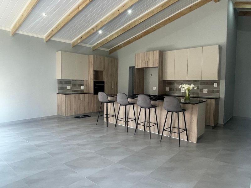 Modern open-plan kitchen featuring sleek cabinetry, a central island with breakfast bar seating, and striking exposed timber ceiling beams.