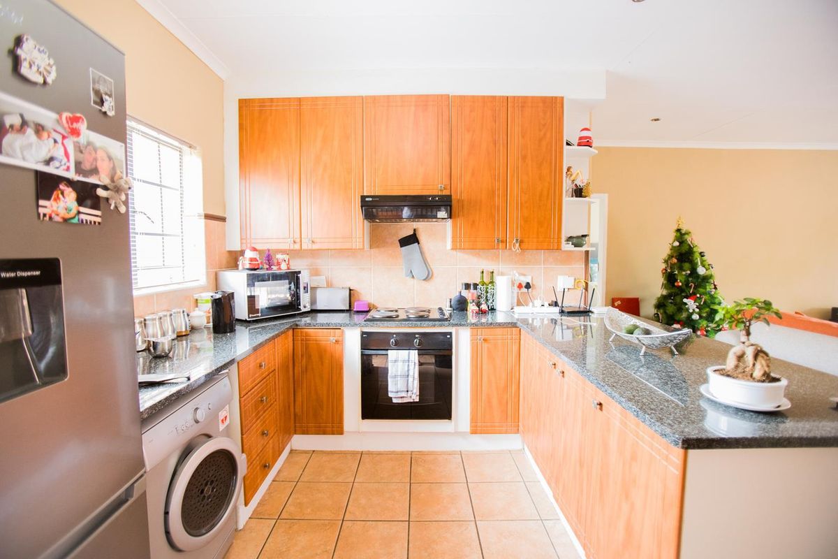 Functional kitchen featuring wooden cabinetry, granite countertops, built-in oven, electric hob, and a breakfast bar, with tiled flooring and backsplash.