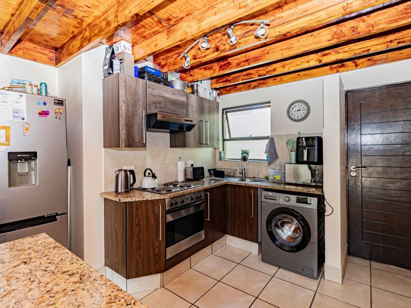 Compact kitchen featuring dark wood cabinetry, granite countertops, built-in oven with hob, and exposed timber ceiling beams, providing a functional and rustic aesthetic.