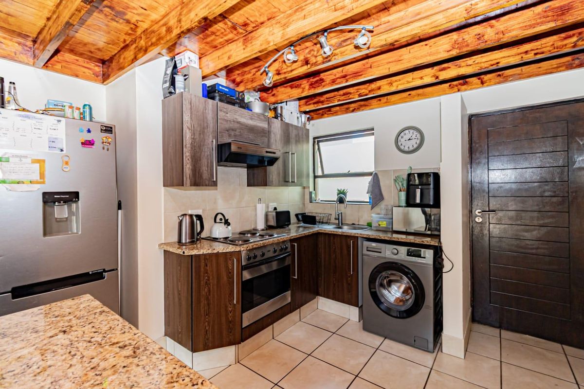 Compact kitchen featuring dark wood cabinetry, granite countertops, built-in oven with hob, and exposed timber ceiling beams, providing a functional and rustic aesthetic.