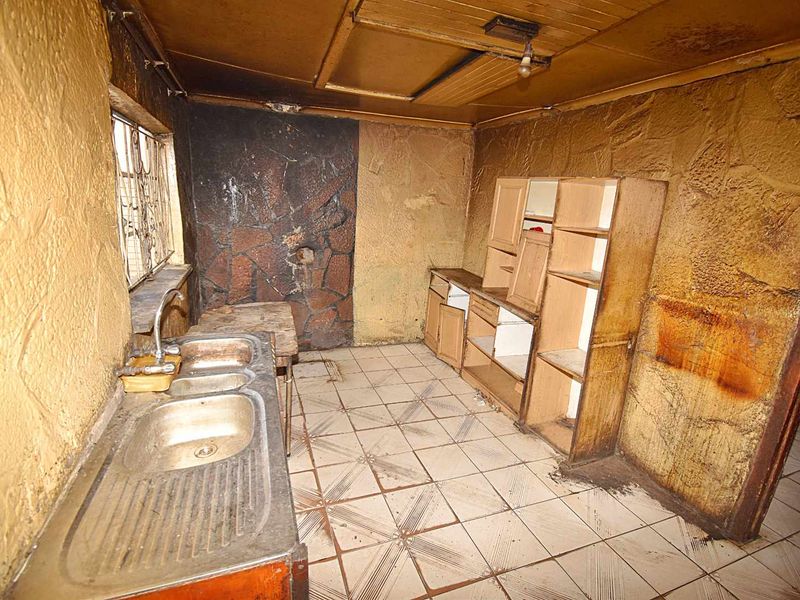 A dilapidated kitchen space featuring a double bowl sink, built-in cabinetry, and heavily stained textured walls, requiring significant renovation and repair.