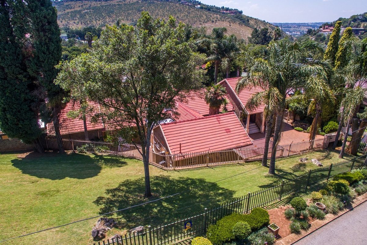 Aerial view of a residential property featuring a tiled roof, extensive landscaped garden, and secure perimeter fencing in a suburban setting.