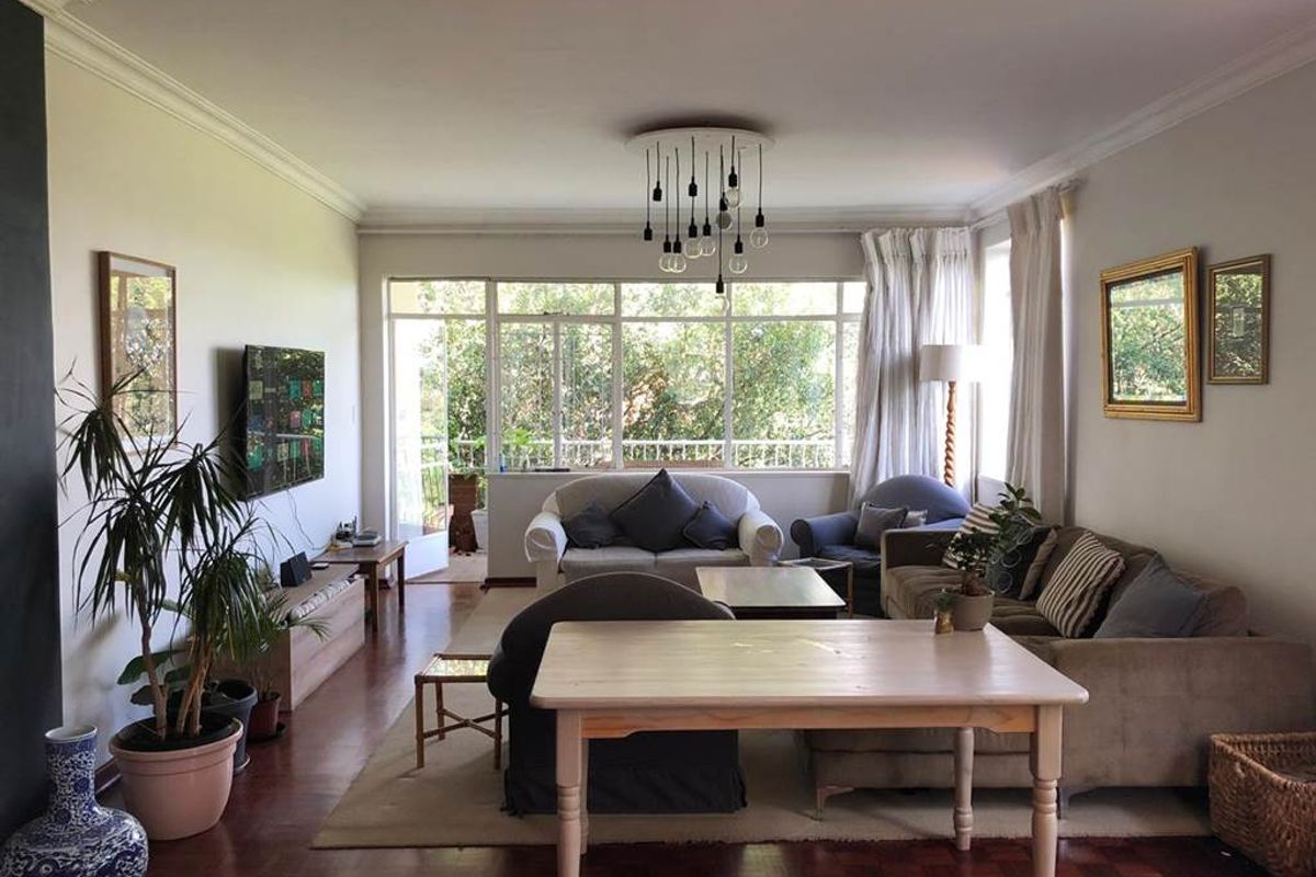 Spacious living room featuring warm parquet flooring, crown molding, and large windows that provide ample natural light and access to the balcony.