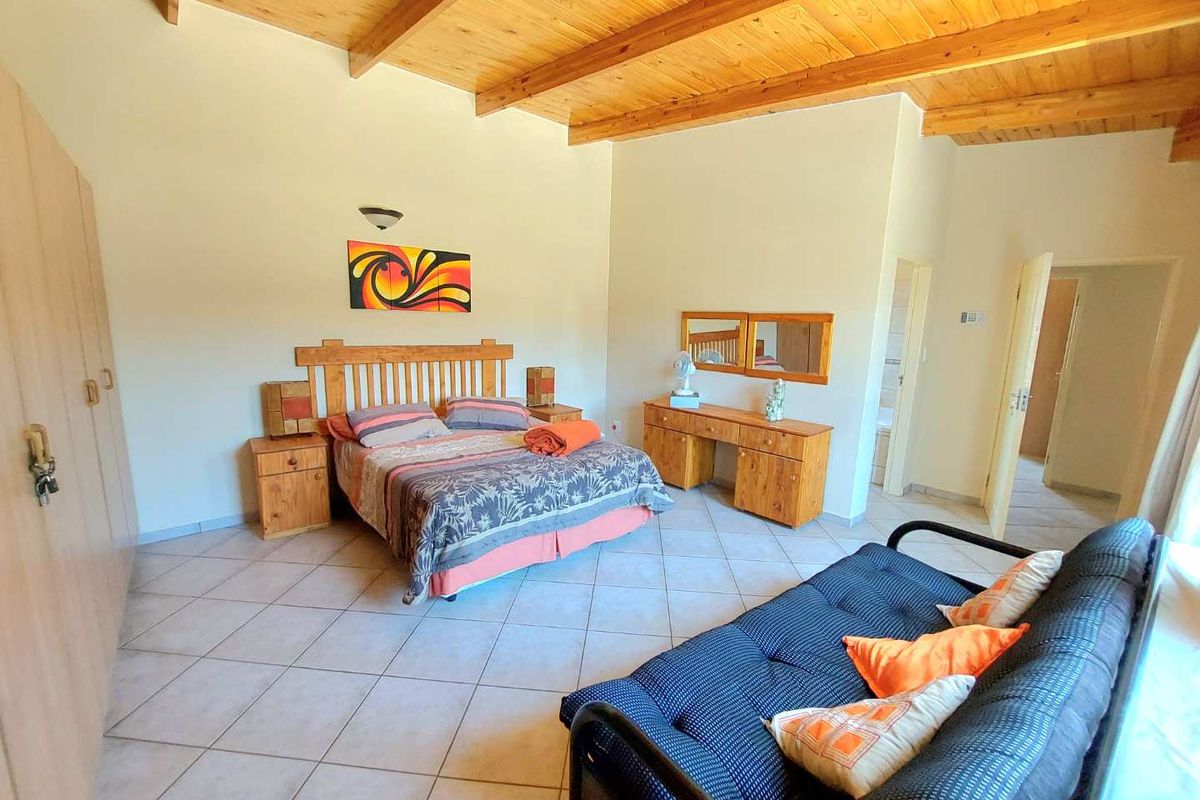 Spacious bedroom featuring high vaulted timber ceilings, tiled flooring, and built-in cupboards, with an adjoining en-suite bathroom.