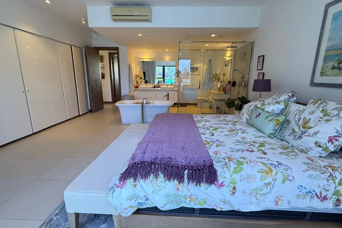Spacious open-plan bedroom featuring an integrated en-suite bathroom with a freestanding bathtub, glass-enclosed shower, double vanity, and extensive built-in wardrobe storage.