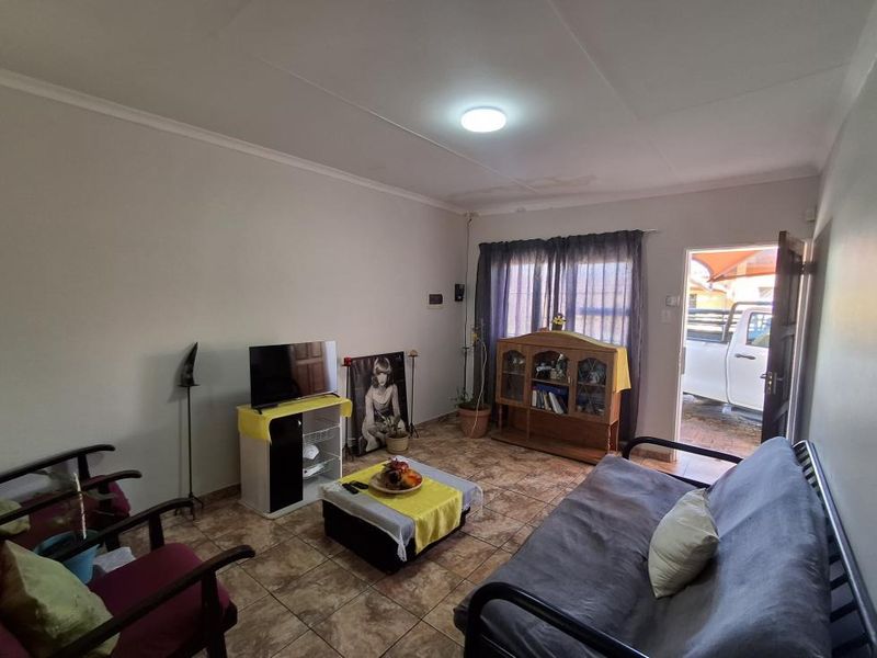 A living room featuring tiled flooring and direct access to the exterior, with visible ceiling water staining requiring attention.