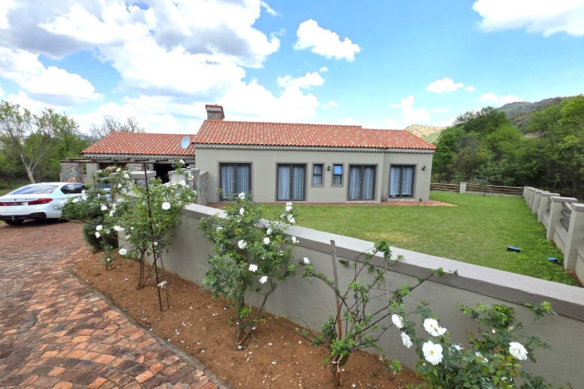 Rear view of a single-story residence featuring terracotta roof tiles, multiple sets of french doors, and a well-maintained lawn with masonry boundary walling.