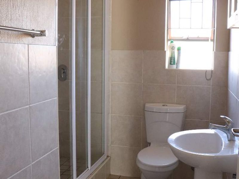 A functional bathroom featuring a shower enclosure, pedestal basin, and toilet, finished with neutral wall and floor tiles.