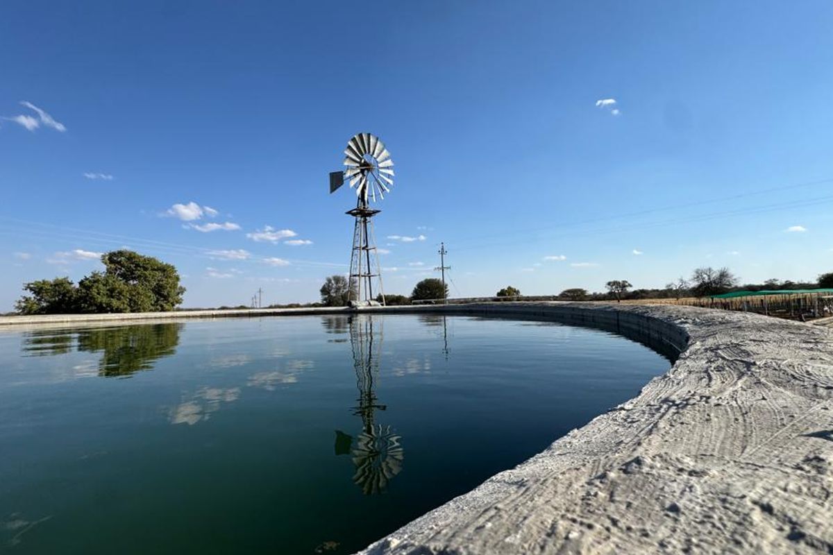 A large circular concrete water reservoir on a farm, featuring a traditional metal windmill in the background under a clear blue sky.
