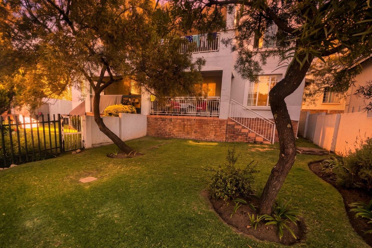 Rear view of the townhouse featuring a private garden, brick retaining wall, and a raised patio area with metal balustrades.