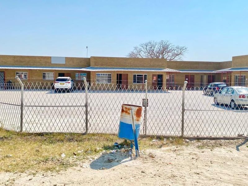 Front view of a single-story commercial property featuring a paved parking lot, secure perimeter fencing, and multiple access points with security bars.