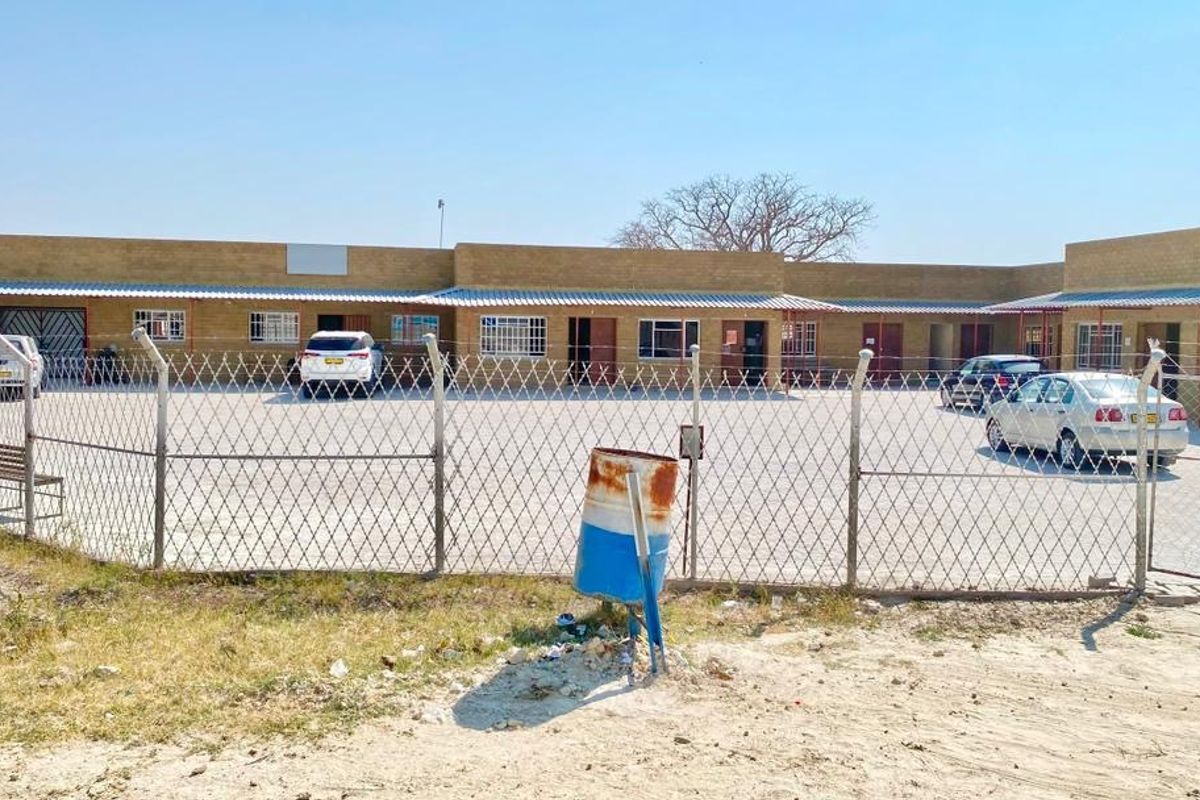 Front view of a single-story commercial property featuring a paved parking lot, secure perimeter fencing, and multiple access points with security bars.