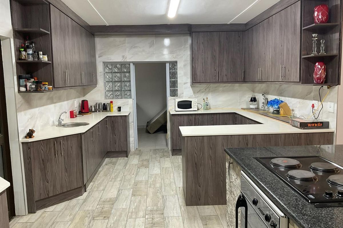 A modern kitchen featuring dark wood-grain cabinetry, white stone countertops, marble-look wall tiles, and a built-in electric stove with a black granite surface.