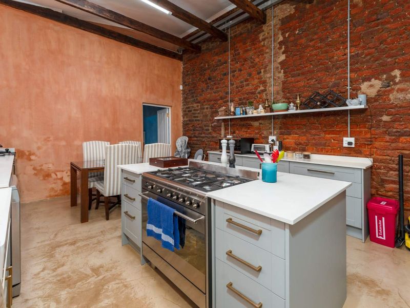 Industrial-style kitchen featuring exposed brick walls, timber ceiling beams, concrete floors, a central island with a gas stove, and modern grey cabinetry.