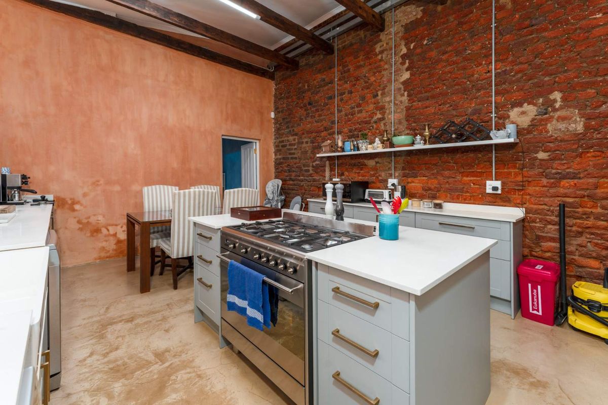 Industrial-style kitchen featuring exposed brick walls, timber ceiling beams, concrete floors, a central island with a gas stove, and modern grey cabinetry.
