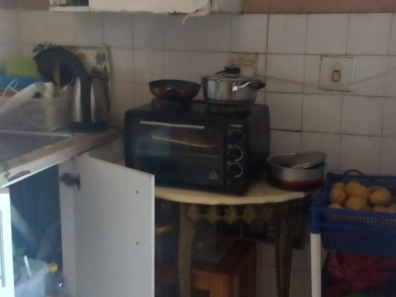A compact kitchen area featuring a tiled backsplash, stainless steel sink, and built-in cabinetry, currently showing signs of wear and requiring maintenance.