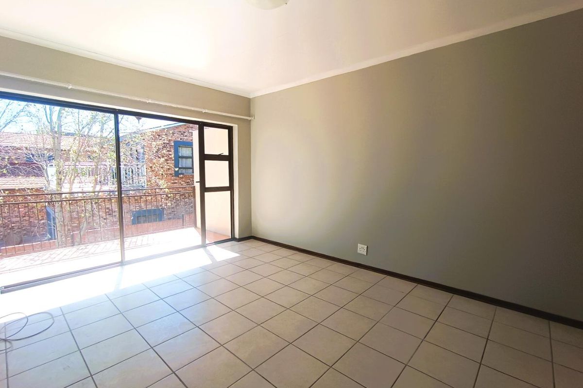 A bright, empty bedroom featuring tiled flooring and a large sliding glass door that opens onto a private balcony.