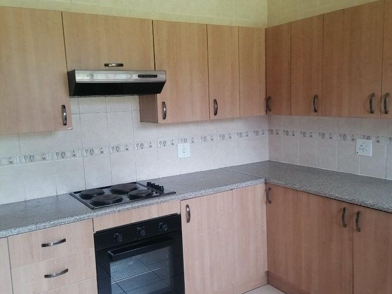 A functional kitchen featuring light wood-look cabinetry, granite-style countertops, built-in oven and hob, and neutral ceramic floor tiling.