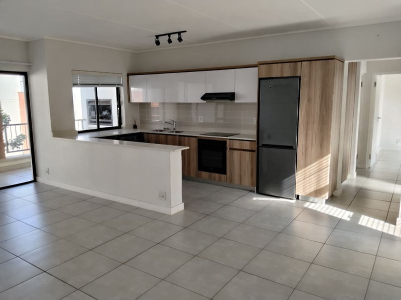 Modern open-plan kitchen featuring sleek wood-tone and white cabinetry, stone countertops, integrated appliances, and tiled flooring, seamlessly connecting to the living area.