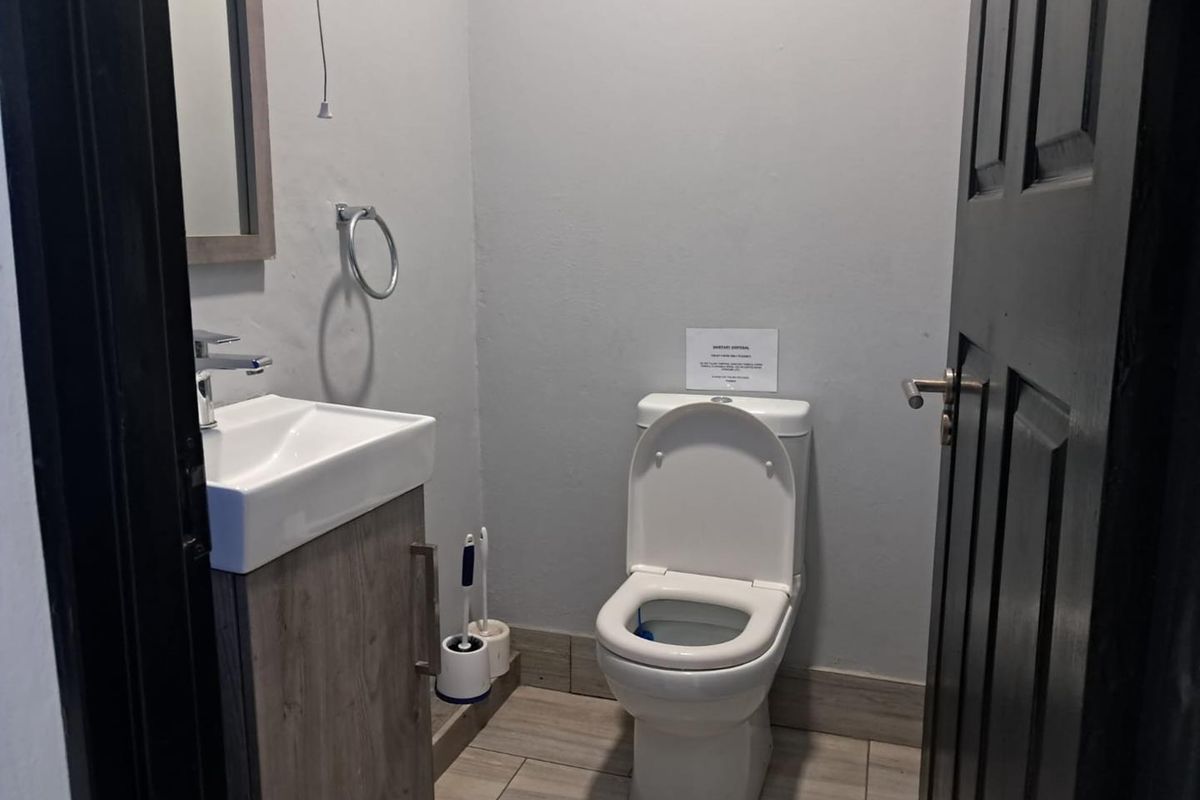 A compact office restroom featuring a modern vanity with integrated basin, a standard toilet, and neutral floor tiling.