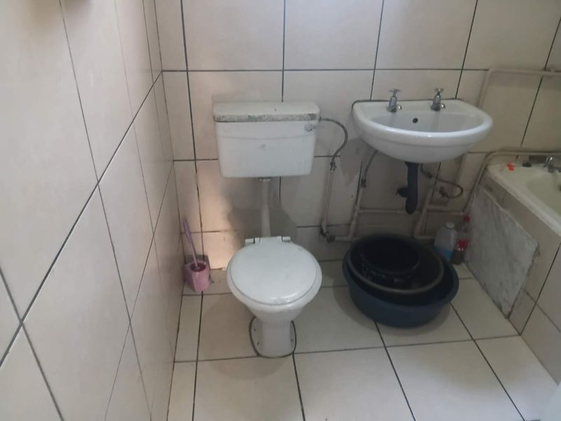 A dated bathroom featuring basic ceramic tiling, a standard pedestal washbasin, flush toilet, and bathtub, requiring modernization and cosmetic updates.