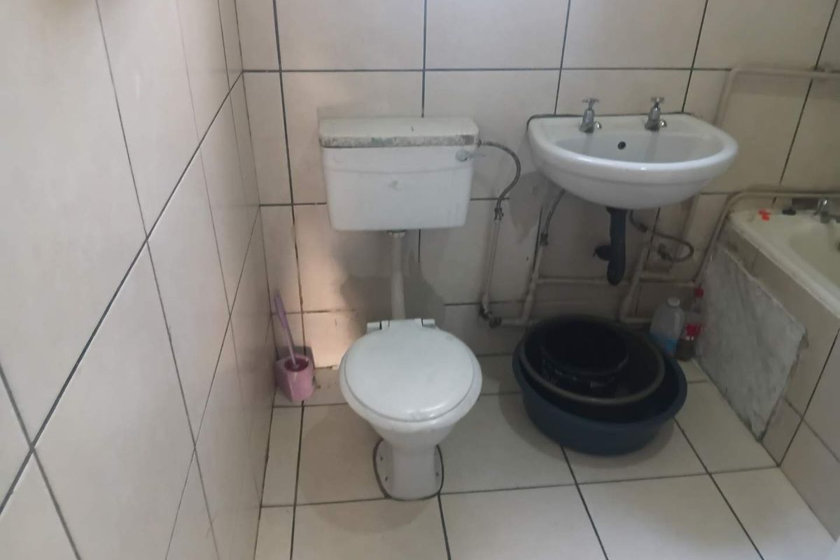A dated bathroom featuring basic ceramic tiling, a standard pedestal washbasin, flush toilet, and bathtub, requiring modernization and cosmetic updates.