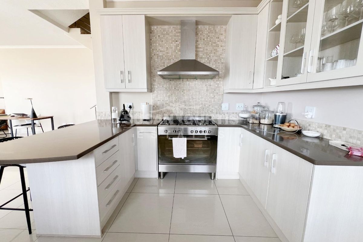 A well-maintained kitchen featuring light-toned cabinetry, a mosaic tile backsplash, stainless steel oven and extractor fan, and a breakfast bar counter.