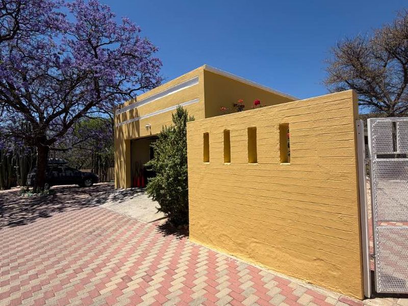Front view of the property featuring a paved driveway, a yellow boundary wall with decorative cutouts, and a garage entrance.