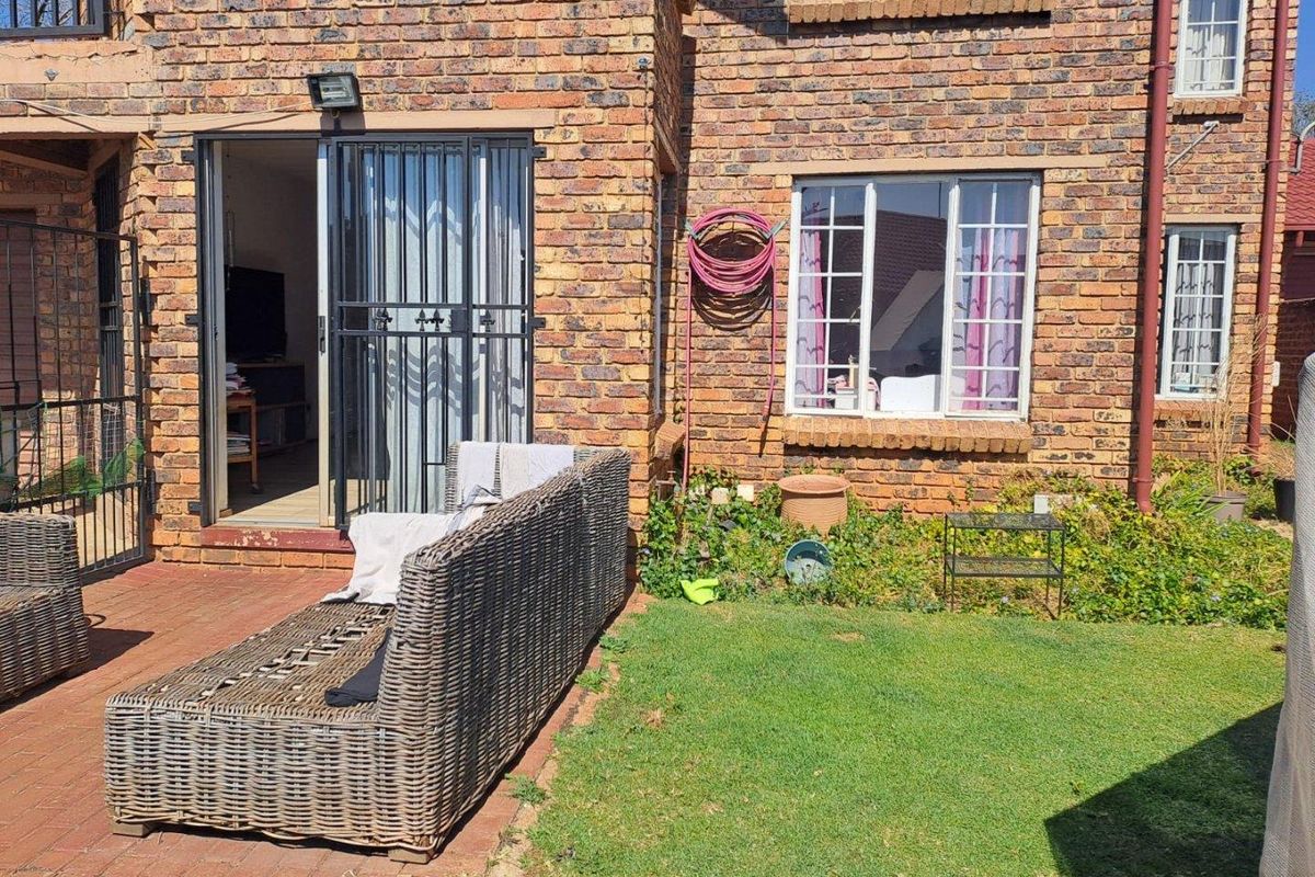 Rear exterior view of the apartment featuring a face brick facade, paved patio area, and a small private lawn.