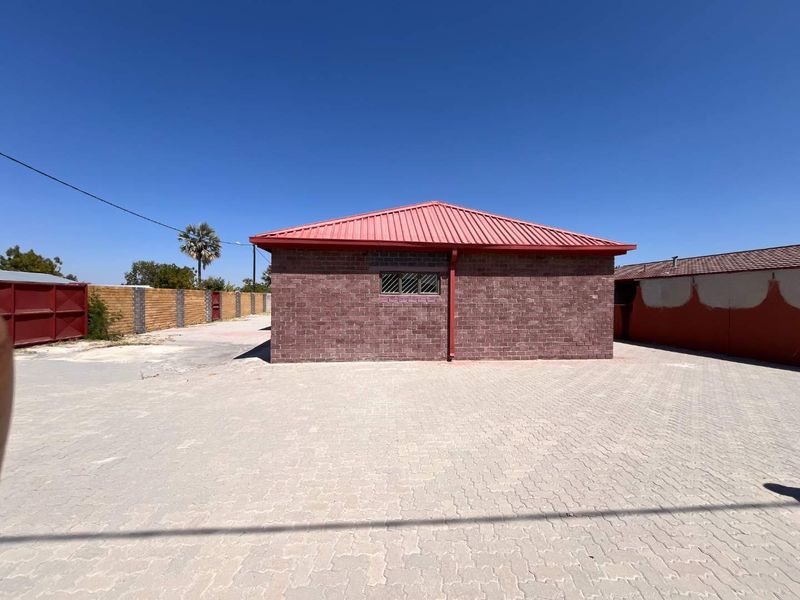 A view of the rear exterior of the property featuring a brick facade, metal roofing, and a spacious paved driveway area.