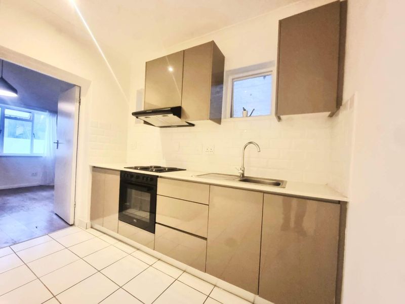 Modern kitchen featuring sleek cabinetry, built-in oven, electric hob, extractor fan, and subway tile backsplash with clean tiled flooring.