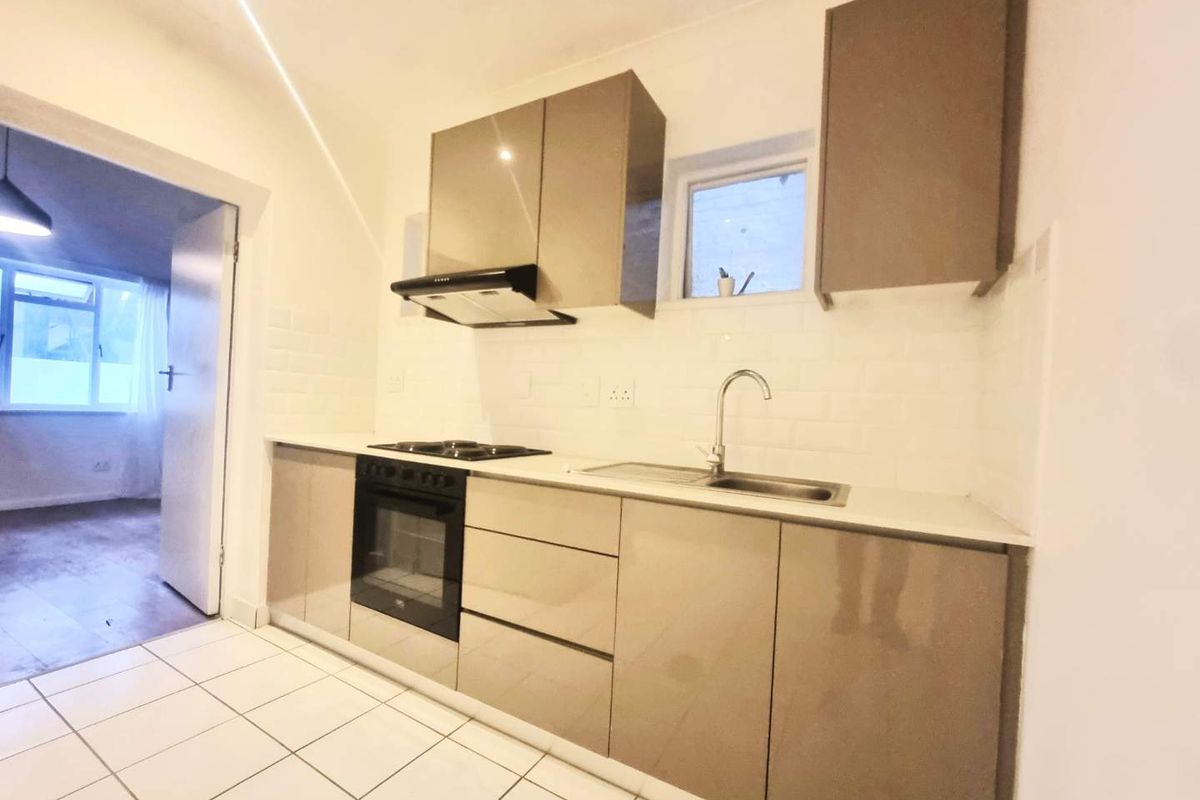 Modern kitchen featuring sleek cabinetry, built-in oven, electric hob, extractor fan, and subway tile backsplash with clean tiled flooring.