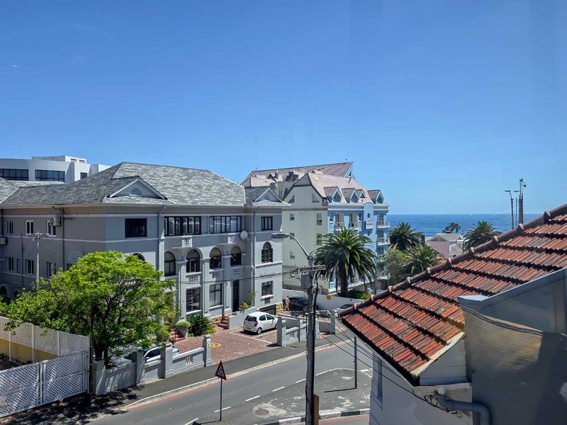 An elevated view overlooking a coastal neighborhood street with surrounding apartment buildings and a glimpse of the ocean in the distance.