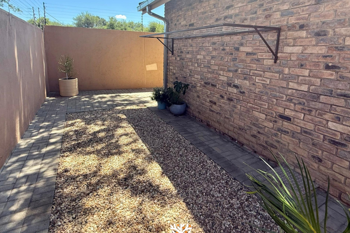 A private rear courtyard featuring a brick-walled boundary, paved pathways, and a gravel garden area with a wall-mounted drying rack.