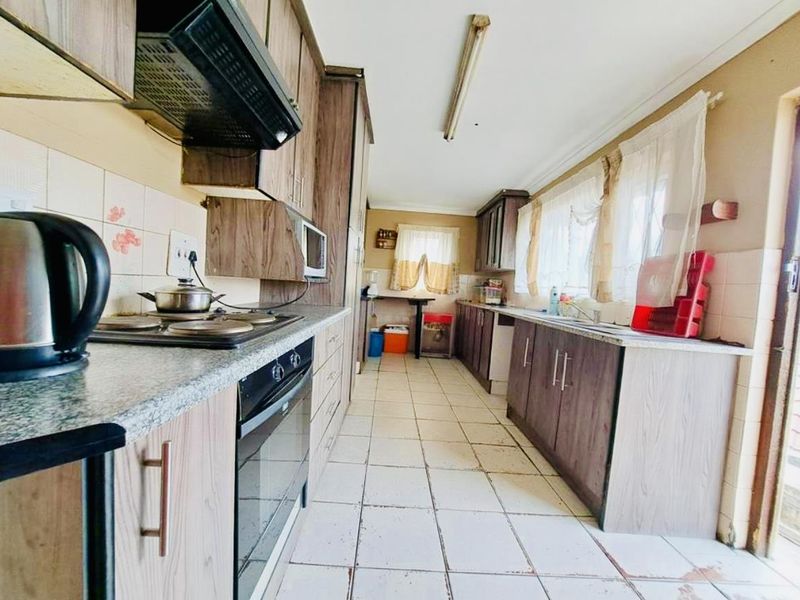 A functional galley-style kitchen featuring wood-look cabinetry, laminate countertops, built-in oven and hob, and tiled flooring throughout.